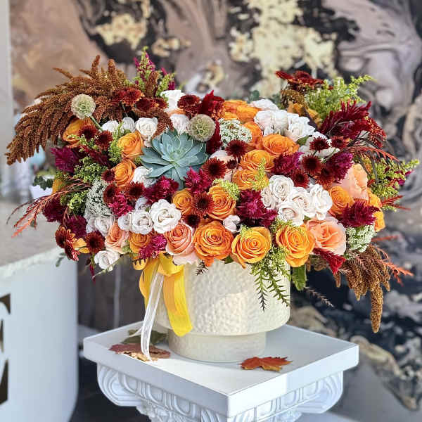 Large bouquet of orange and white roses with burgundy accents in a white vase