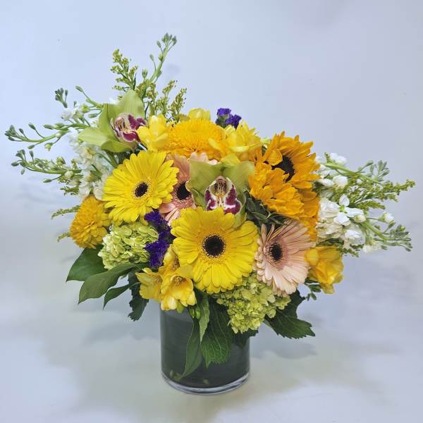 Yellow mixed bouquet in a glass vase with gerbera daisies and sunflowers