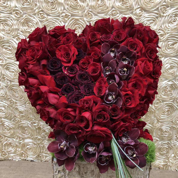 Heart-shaped bouquet of red roses with dark orchids on a textured backdrop