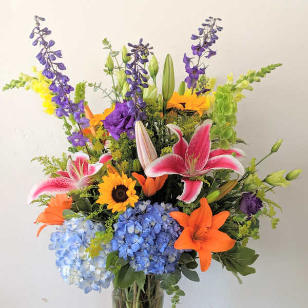 Colorful mixed bouquet in a clear glass vase with lilies, hydrangeas, and sunflowers