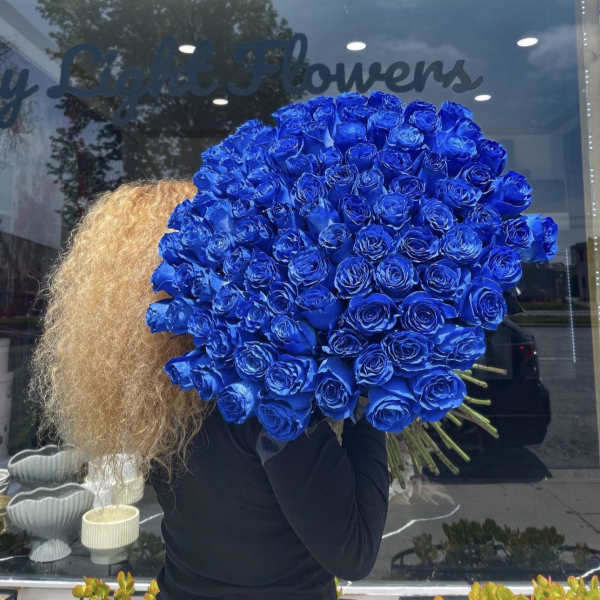 Large bouquet of vivid blue roses held in front of a shop window