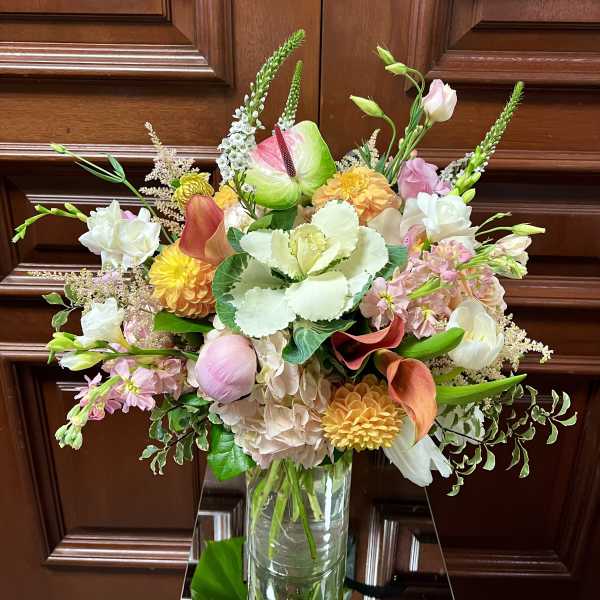 Tall mixed bouquet of pink, peach, yellow, and white flowers in a clear glass vase.