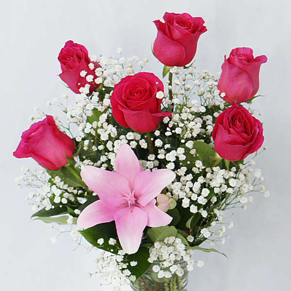 Pink roses and a lily in a glass vase with white baby's breath