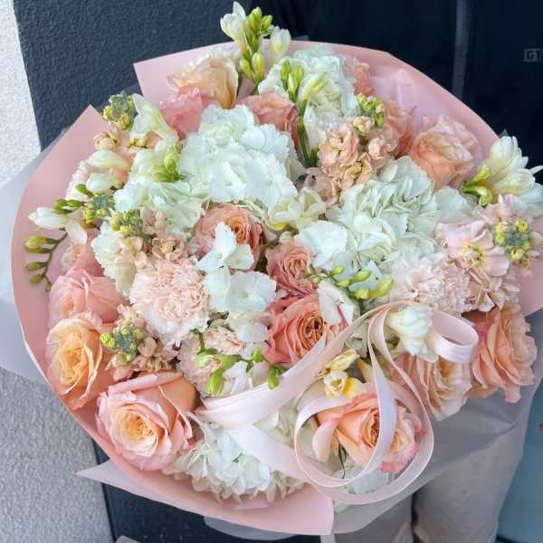 Large pastel bouquet of roses, hydrangeas, and white blooms wrapped in pink paper