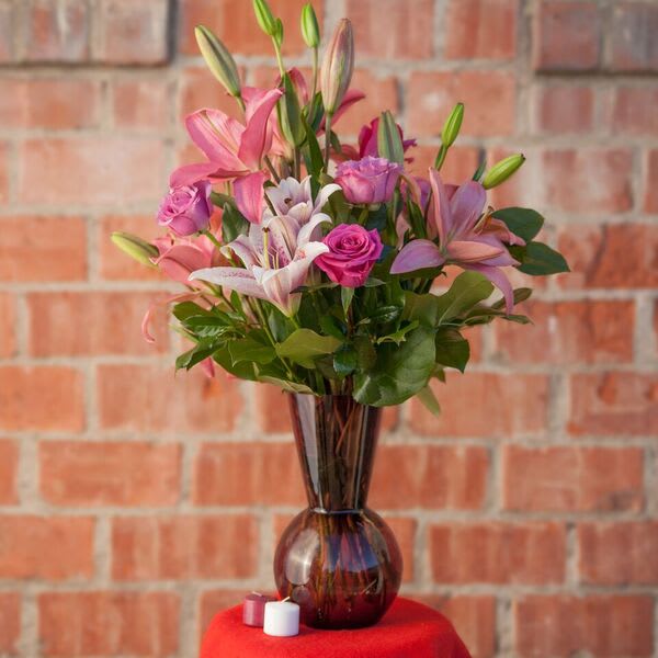 Pink lilies and roses in a dark glass vase with two small candles