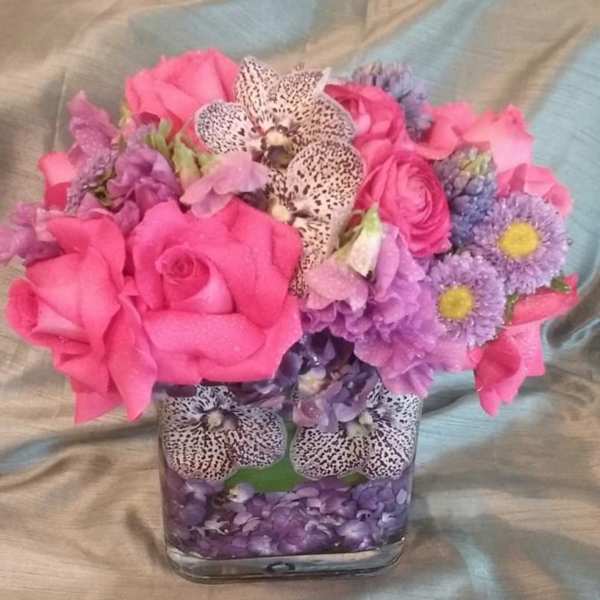 Pink and purple bouquet in a square glass vase with spotted orchids