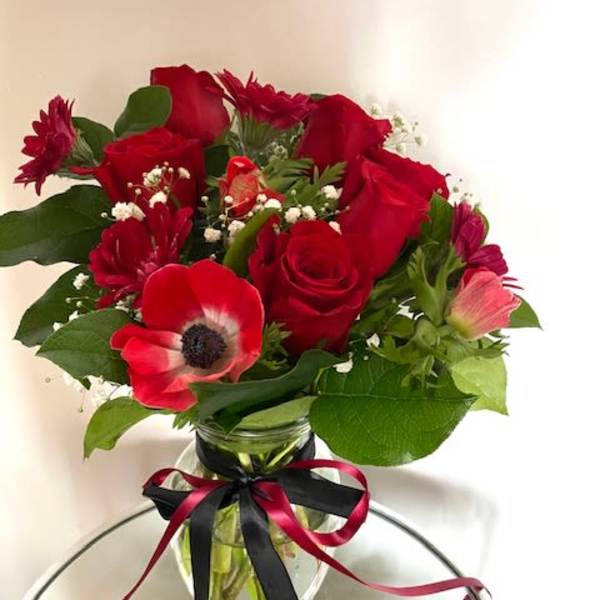Red roses and mixed blooms arranged in a glass vase with ribbon