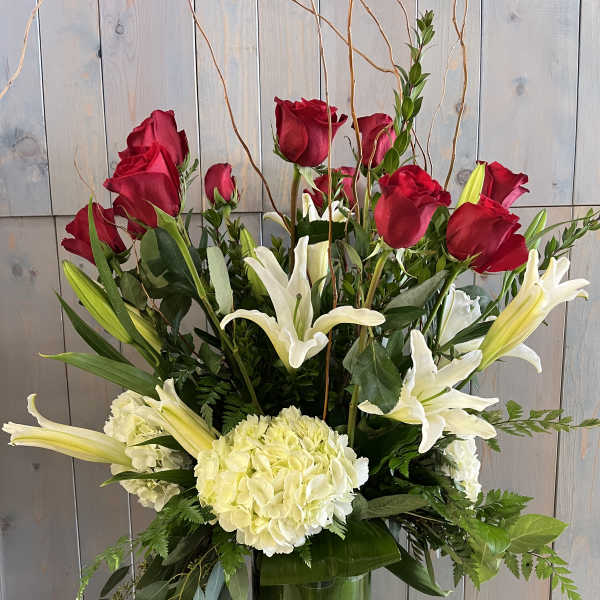 Red roses and white lilies in a tall glass vase with greenery