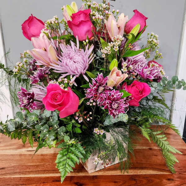 Pink roses and lilies arranged in a white box with mixed greenery