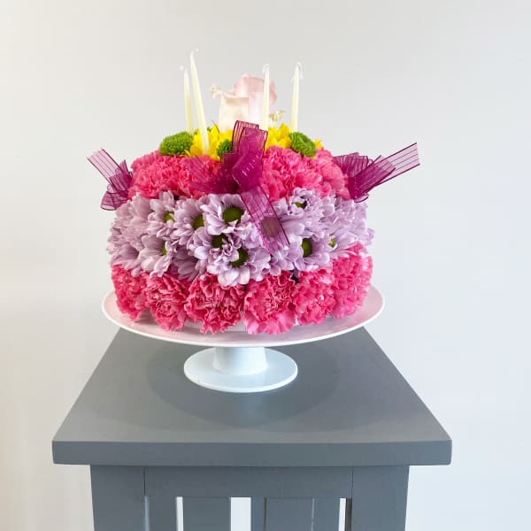 Pink and lavender flower cake with candles on a white pedestal stand