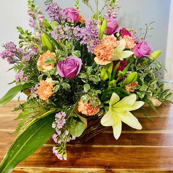 Mixed bouquet with pink roses, lilies, and peach carnations in a basket