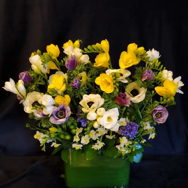 Yellow, white, and purple flowers arranged in a green vase