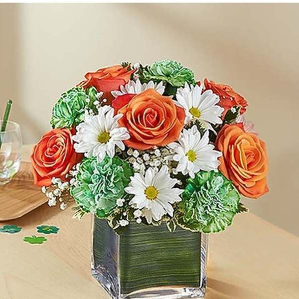 Bouquet of orange roses, white daisies, and green carnations in a square glass vase