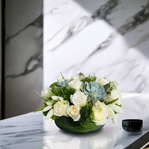 White roses and succulents arranged in a low green bowl