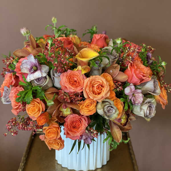 Mixed bouquet of orange, coral, and lavender flowers in a white vase