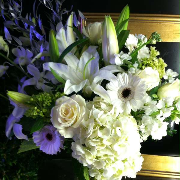 Tall white floral arrangement with lilies, roses, hydrangeas, and gerbera daisies in a clear glass vase