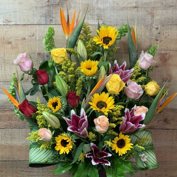 Tall mixed bouquet with sunflowers, roses, lilies, and bird of paradise in a vase
