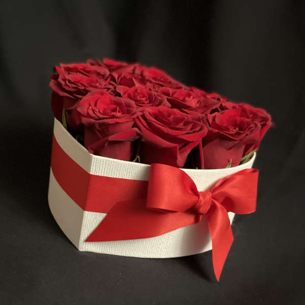 Red roses arranged in a white heart-shaped box with a red ribbon