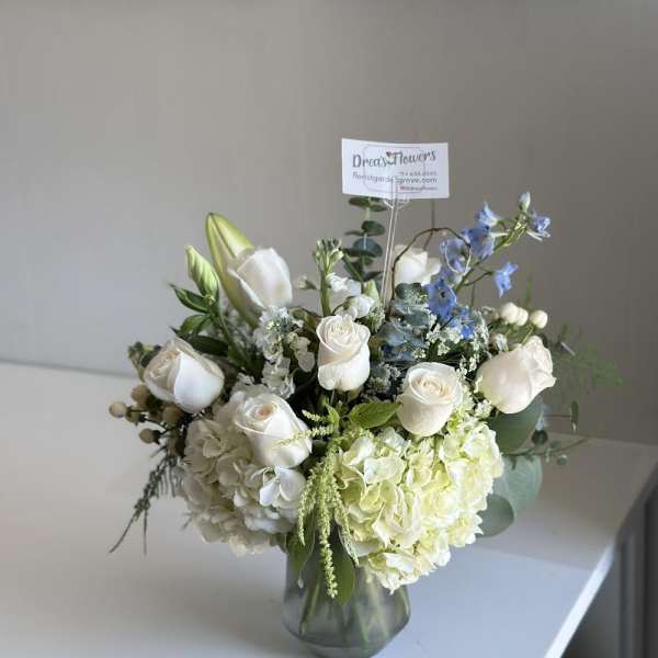 White roses and hydrangeas in a glass vase with blue accents