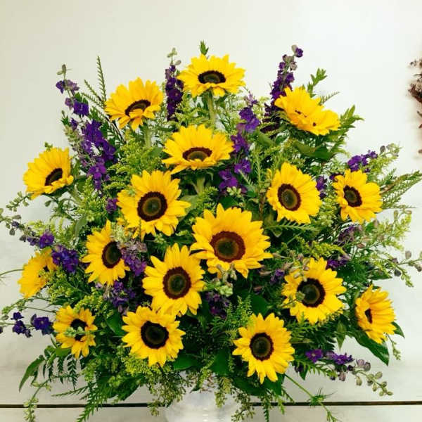 Bright sunflower arrangement in a white vase with purple accents