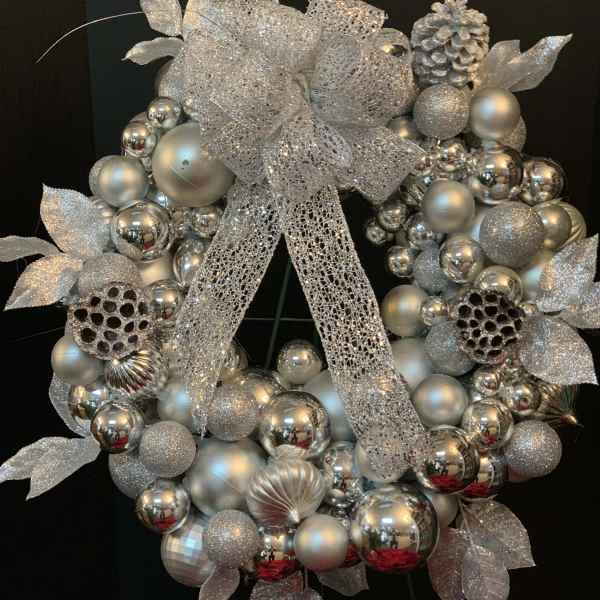 Silver decorative wreath with glittery ornaments and a large mesh bow