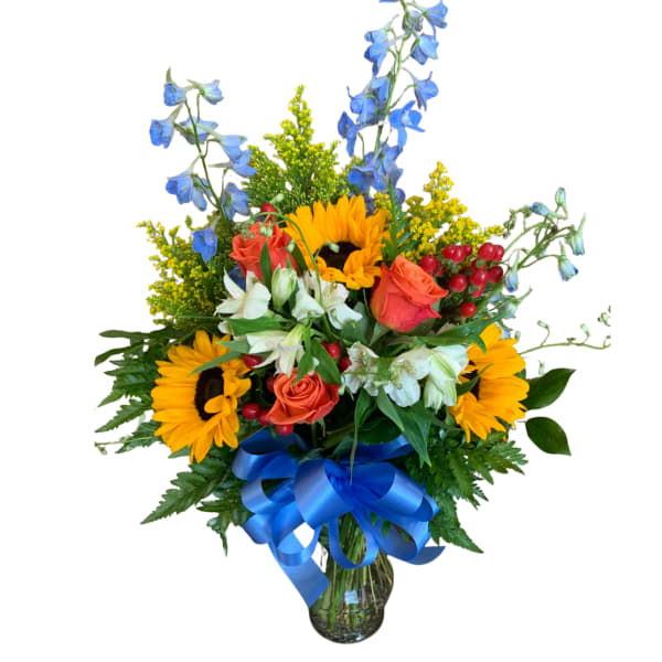Bouquet of sunflowers, roses, and blue flowers in a glass vase with a blue ribbon