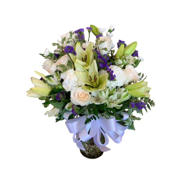 Bouquet of white lilies, roses, and purple filler flowers in a glass vase
