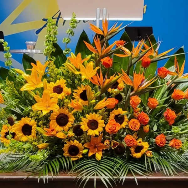 Large yellow and orange altar-style flower arrangement with sunflowers, lilies, roses, and birds of paradise.