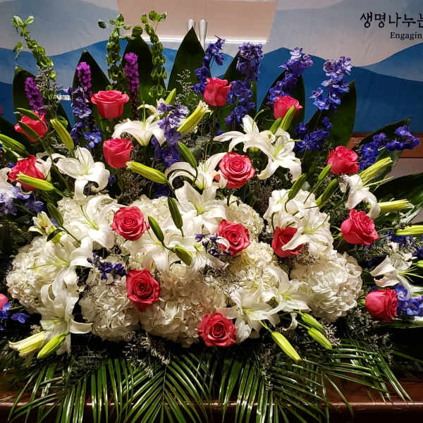 Large altar-style arrangement of white lilies and hydrangeas with red roses and blue delphinium in a fan shape