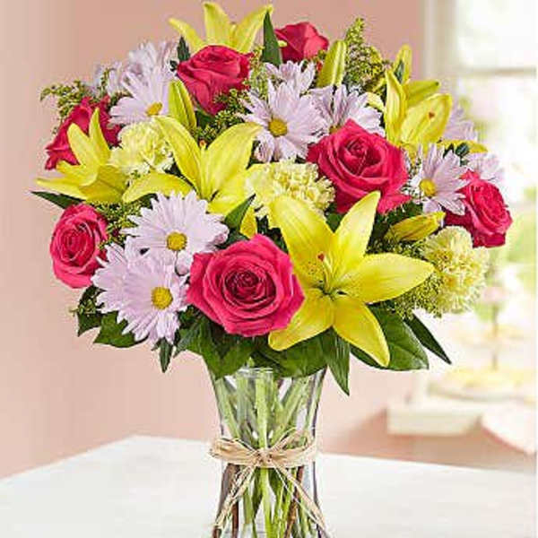 Bouquet of pink roses, yellow lilies, and pale daisies in a glass vase