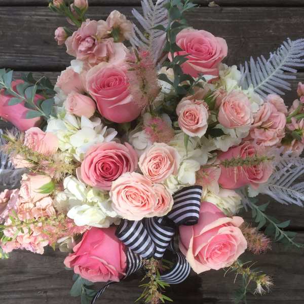 Pink roses and pale blooms arranged with a striped ribbon on wood