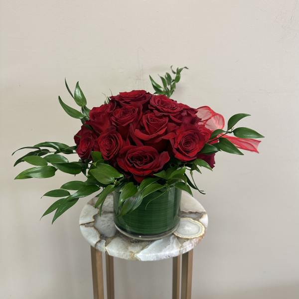 Red roses arranged in a green vase with glossy foliage