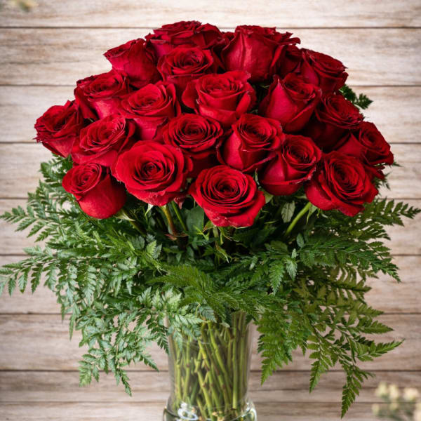 Bouquet of red roses in a clear glass vase with fern foliage