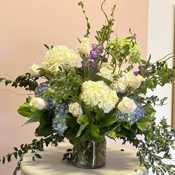 White roses and hydrangeas in a glass vase with trailing greenery
