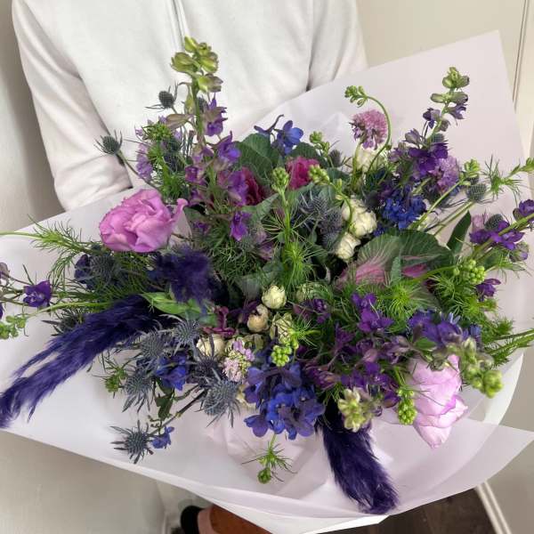 Handheld bouquet of purple and blue flowers wrapped in white paper