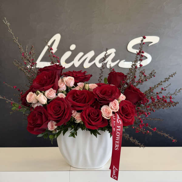 Red and blush roses arranged in a white vase with a red ribbon