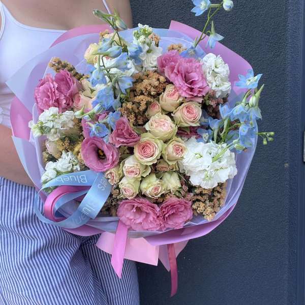 Handheld bouquet of pink and white roses with blue flowers wrapped in pastel paper