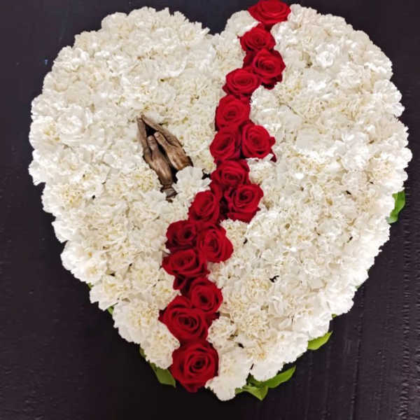 Heart-shaped white floral tribute with a red rose cross and praying hands