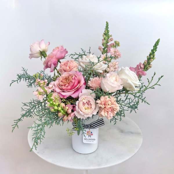 Pink and white roses arranged in a white vase with airy greenery