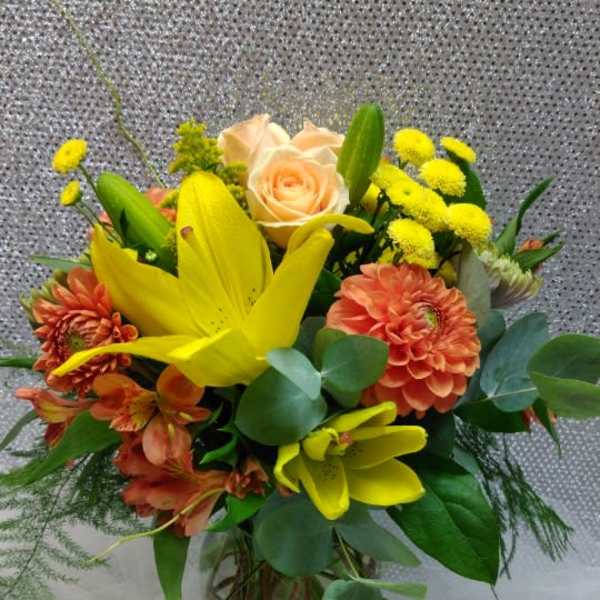 Mixed bouquet with yellow lilies, peach roses, and orange blooms in a glass vase