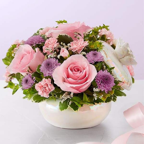 Pink roses and purple daisies arranged in a white bowl vase
