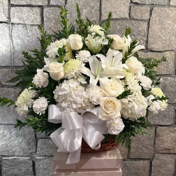 White floral arrangement with roses, lilies, and chrysanthemums in a basket with a ribbon