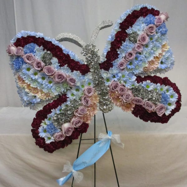 Butterfly-shaped floral standing spray with pink roses and blue daisies