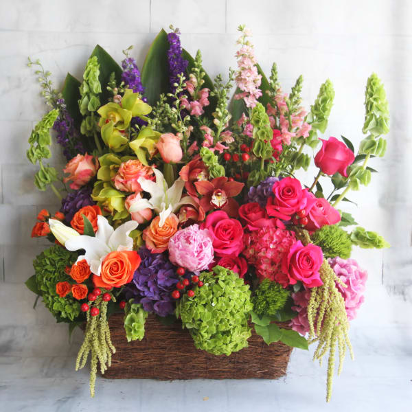 Large mixed flower arrangement in a rectangular basket with pink, orange, purple, and green blooms