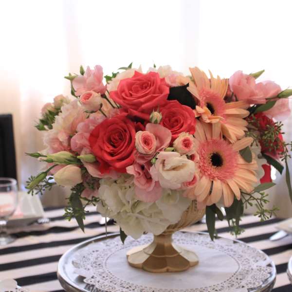 Pink and coral floral centerpiece in a gold vase on a table