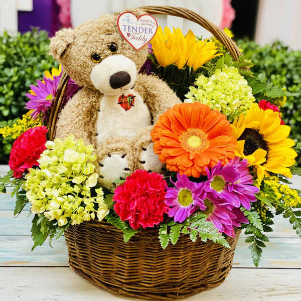 Basket arrangement with a teddy bear surrounded by colorful flowers