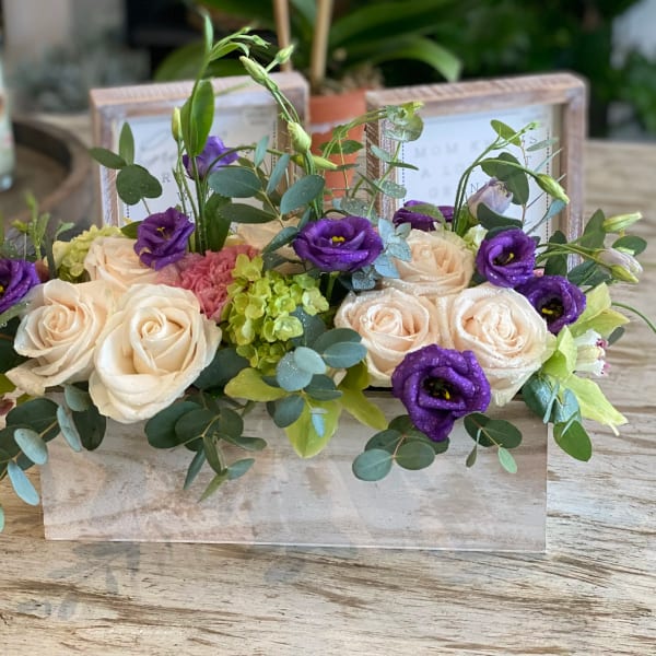 Cream roses and purple blooms arranged in a low wooden box