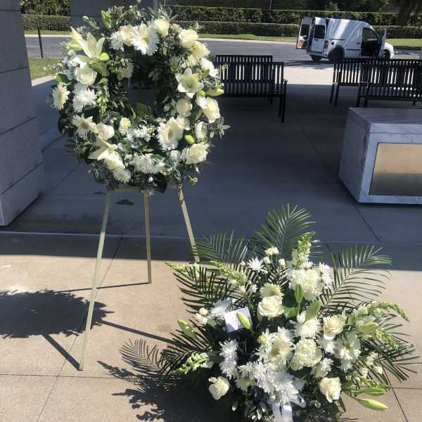White floral funeral wreath on an easel beside a matching floor spray
