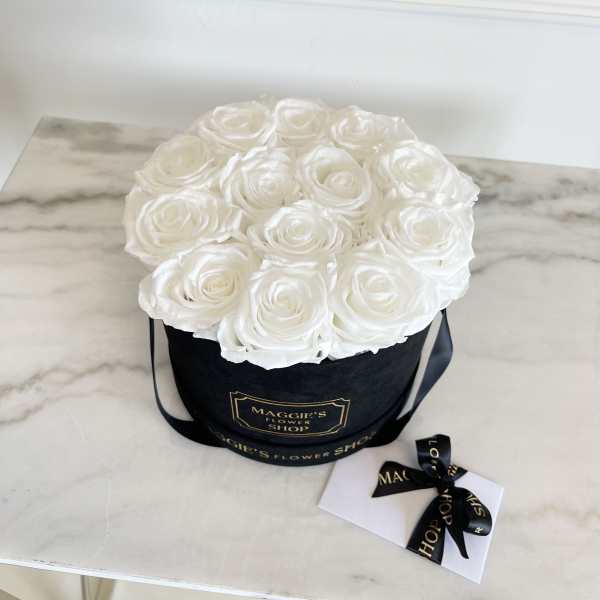 White roses arranged in a black round box with a ribbon and card