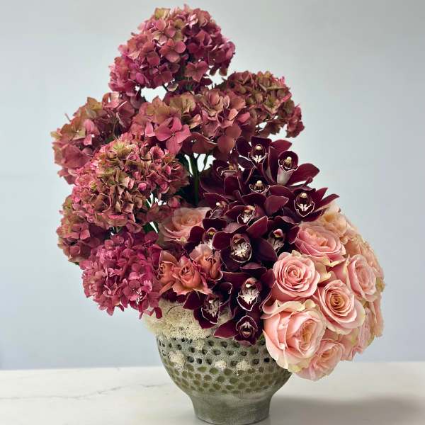 Pink hydrangeas, roses, and dark orchids in a textured vase